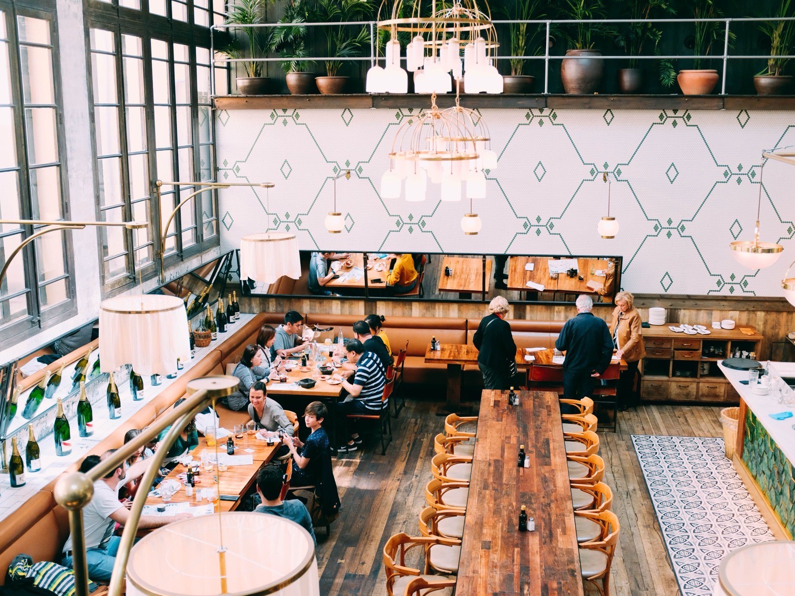 Diners at long communal tables inside a restaurant with tall windows